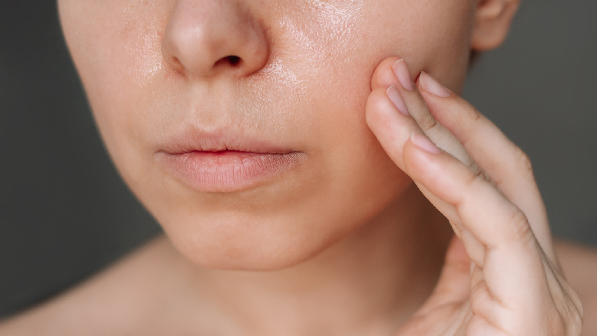 Close-up of a woman gently rubbing skincare product onto her cheek with her fingertips, showing natural skin texture and hydration.